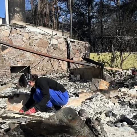 Photo of a relief worker sorting through the wreckage of a burnt home